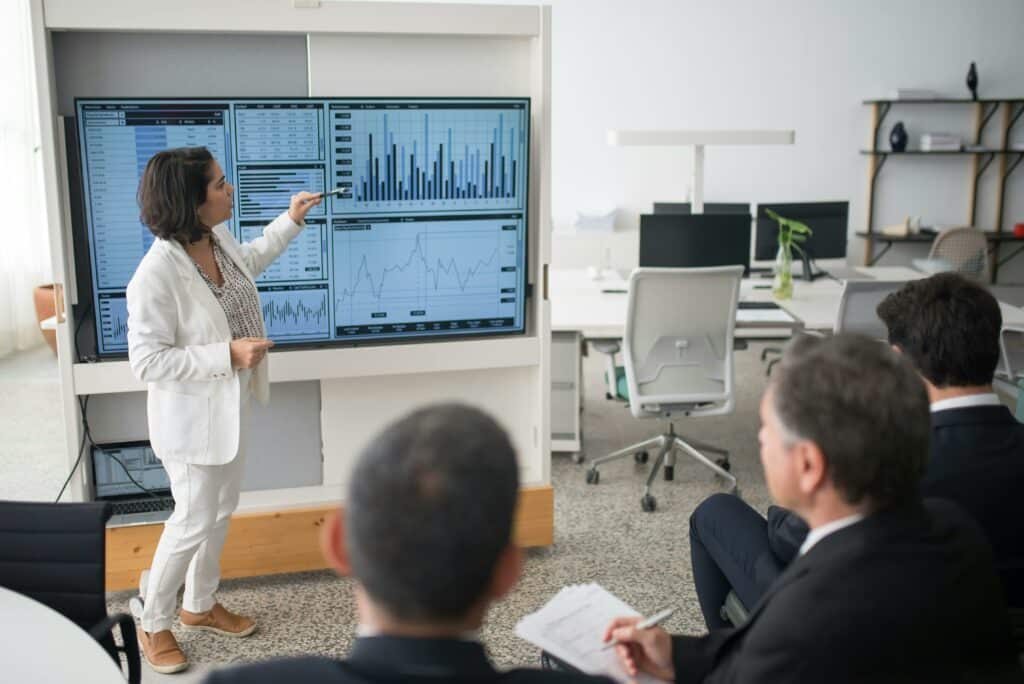 Écrans interactifs : révolutionner les réunions et la collaboration A woman presents data on a screen to a group of colleagues in an open office environment.